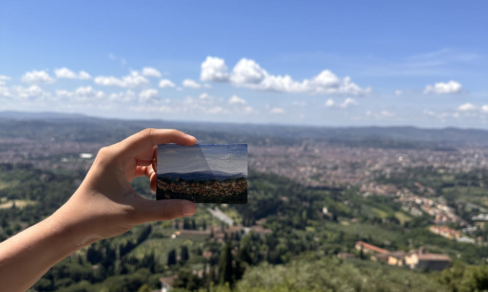 hand holding a small painting in front of a landscape in Florence
