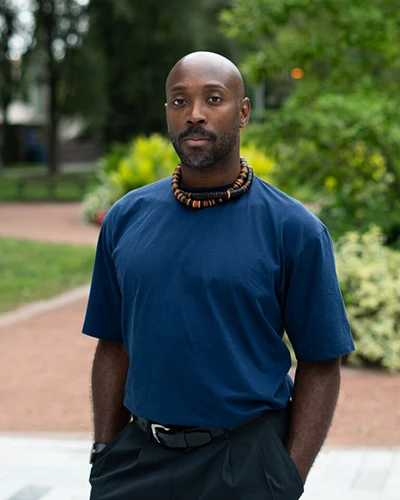 Damon D. Green, in a blue t-shirt, stands with park-line greenery in the background