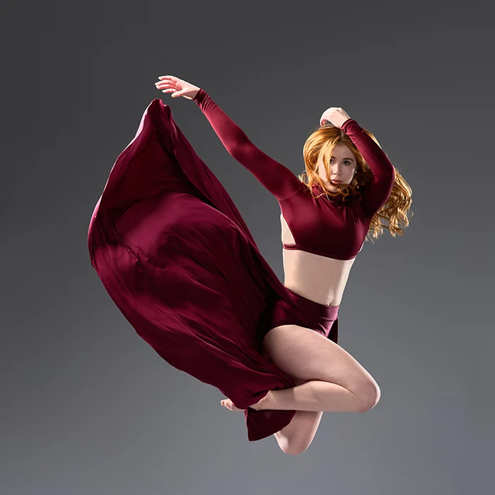 A female dancer in a dramatic red dress is captured mid-jump