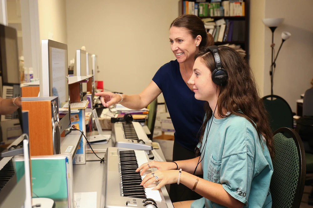 An instructor works with a young musician at piano station in the computer lab