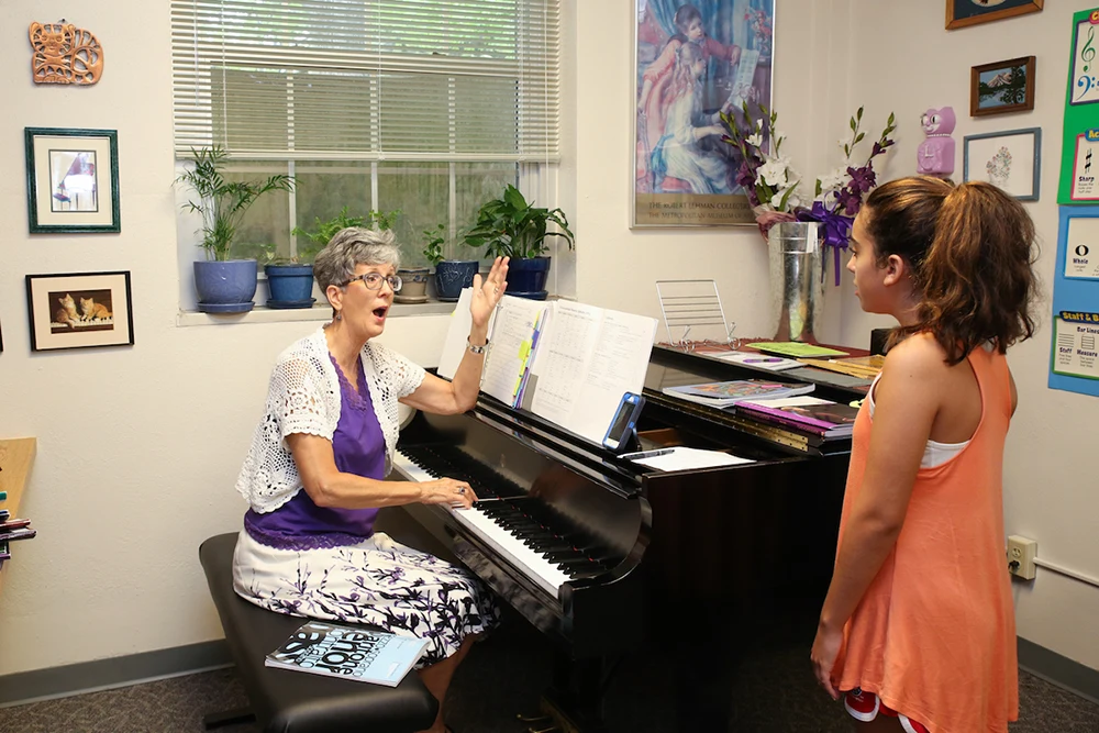 An instructor seated at a piano gives voice instruction to a young student