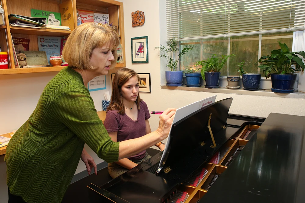 A teacher writes a note on sheet music during a piano lesson