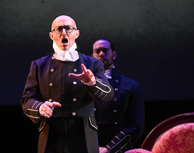 Corey Trahan, dressed in a period costume with glasses, signs on stage