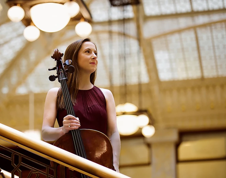Juliette Herlin, in a maroon dress, stands with her cello