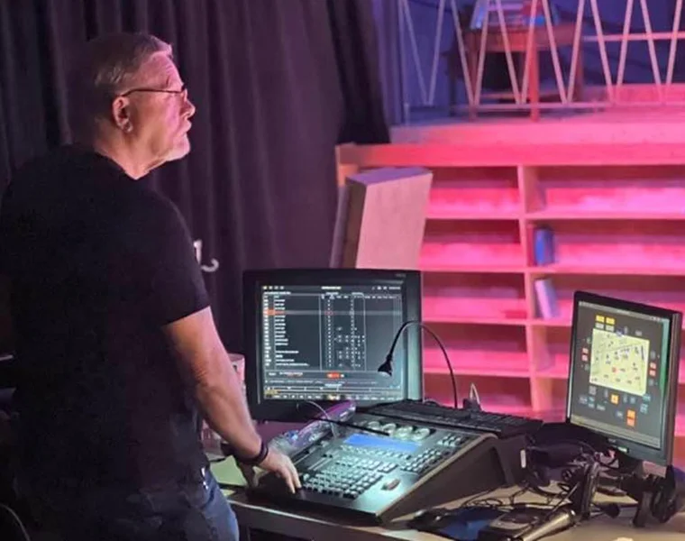 Michael Skinner stands at the lighting console and looks toward the stage