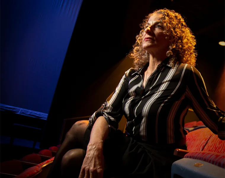 Suki John, seated in a theatre chair, looks off-camera